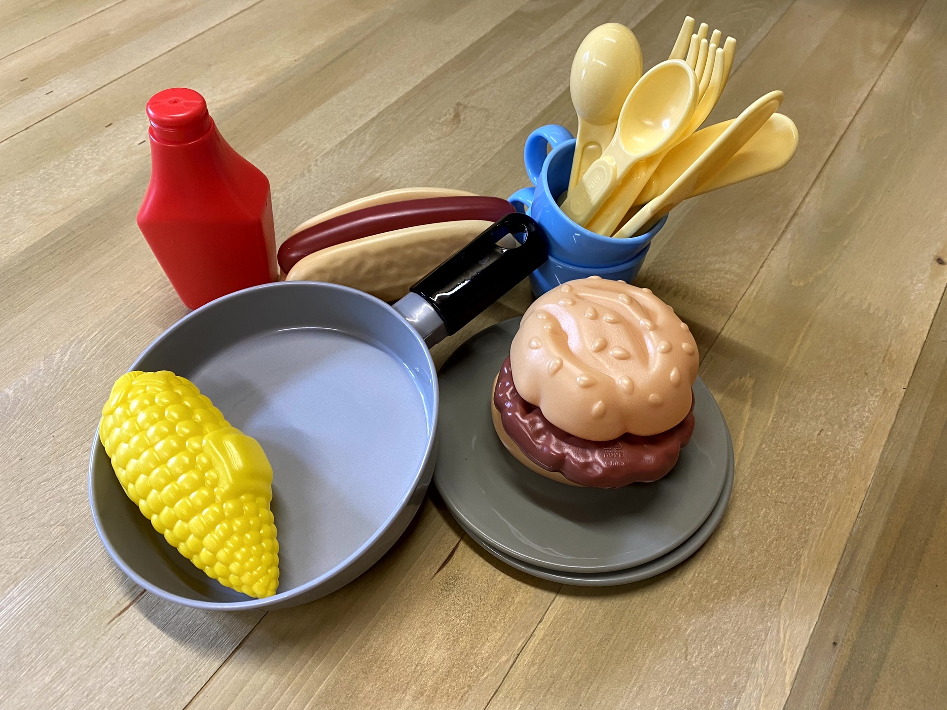 Food Accessory Pack includes Hotdog, Burger/bun, corn, ketchup, 2 cups, frying pan, 2 plates, 2 knifes, forks, spoons. Image